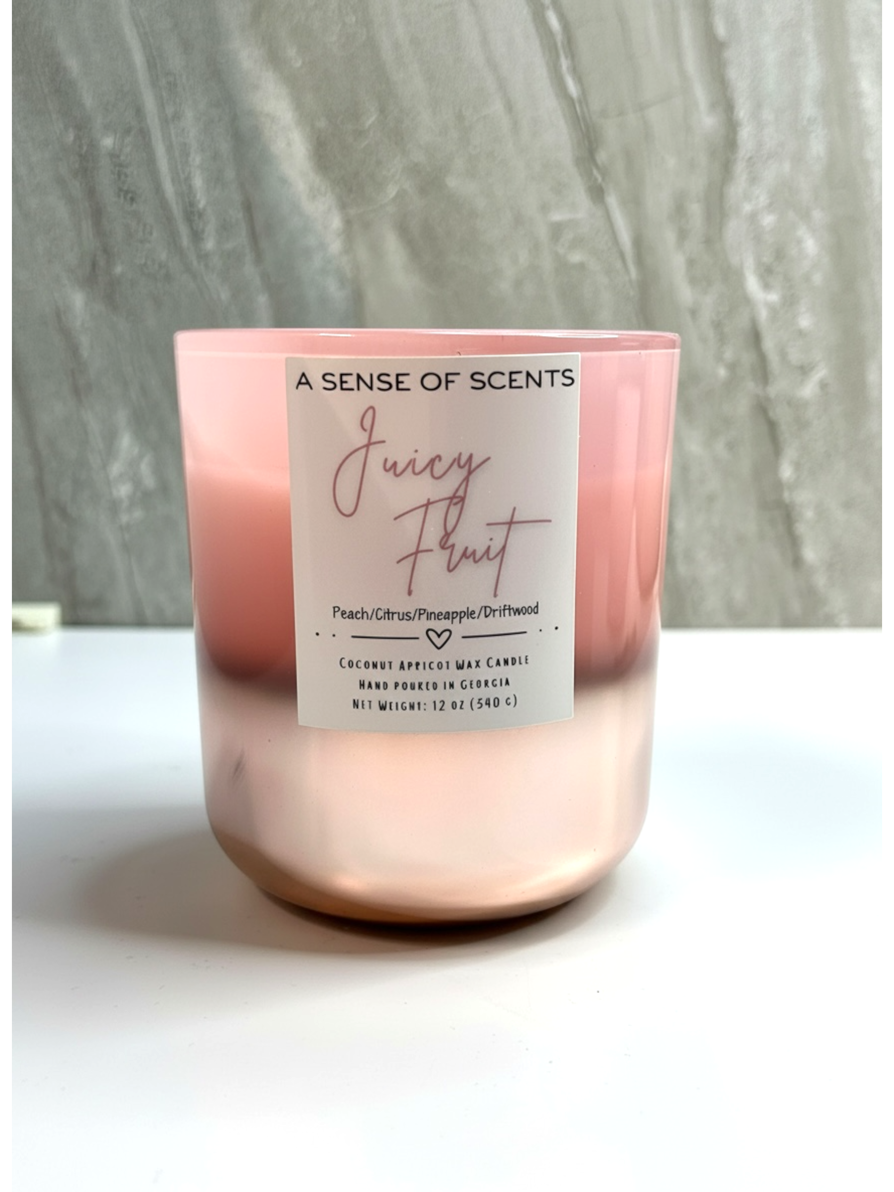 Pink candle labeled 'Juicy Fruit' on a white surface