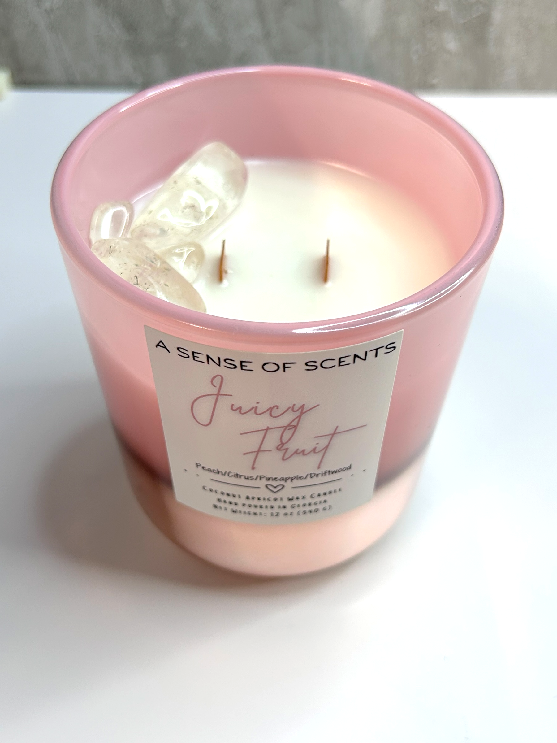 Pink candle labeled 'Juicy Fruit' in a jar on a white surface