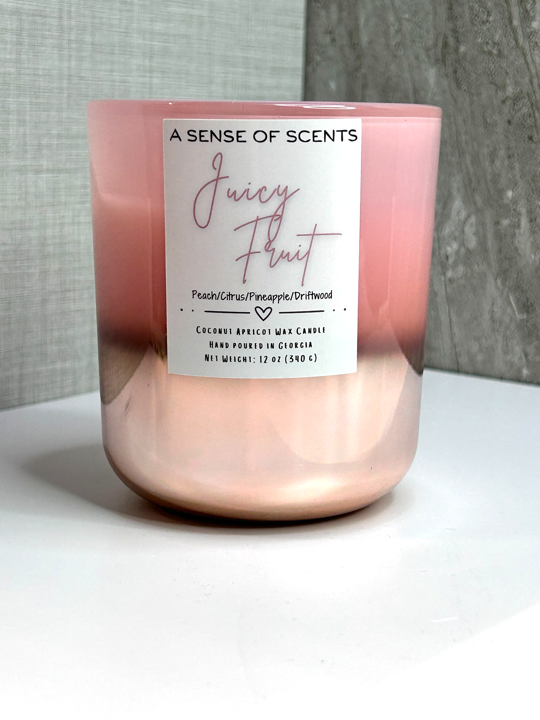 Pink candle labeled 'Juicy Fruit' on a white surface