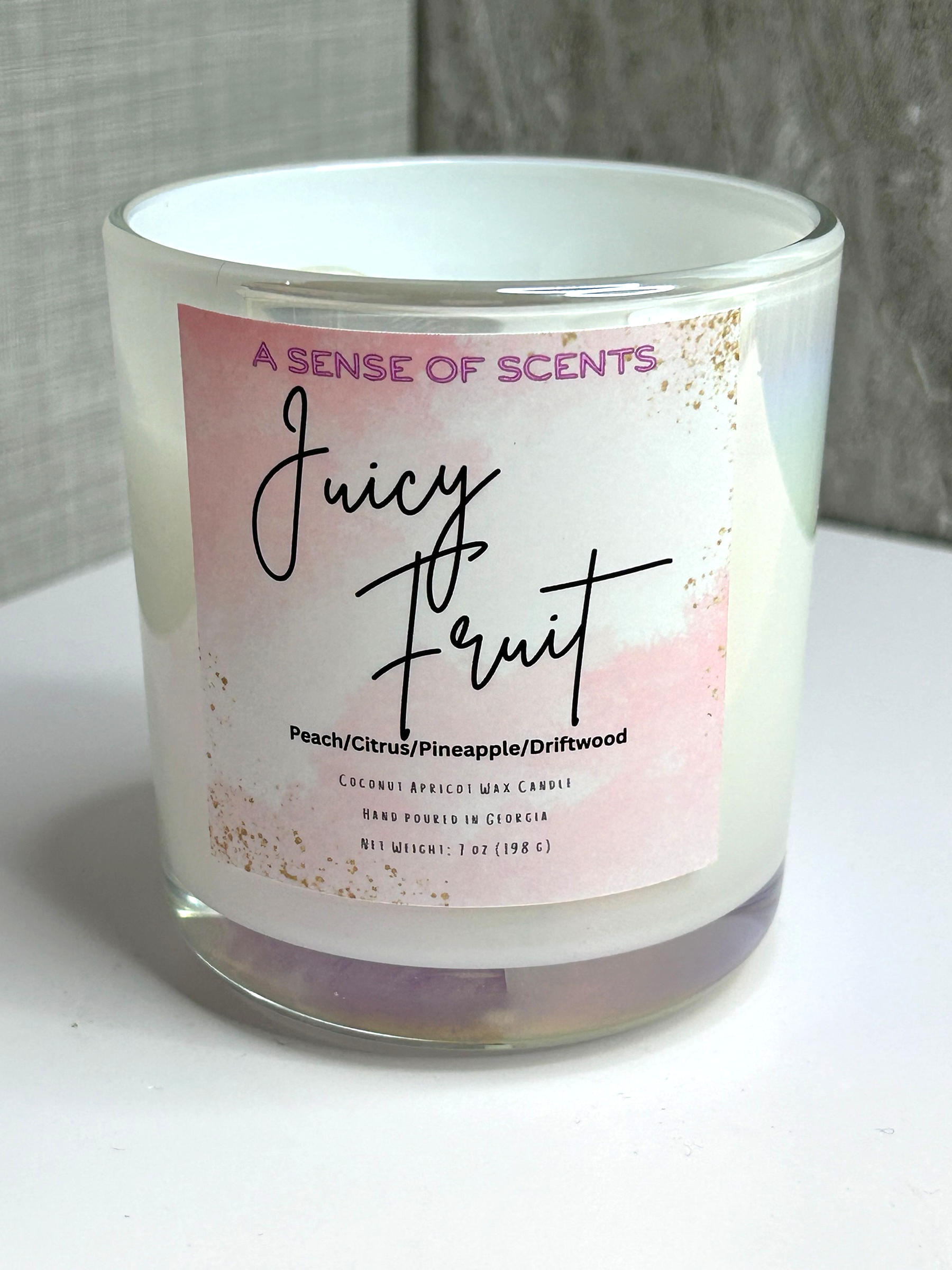Candle with 'Juicy Fruit' label on a white surface and gray background