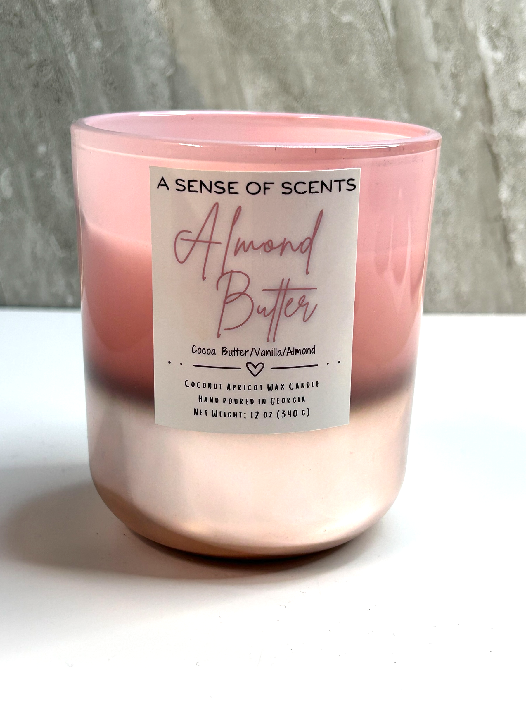 Pink candle labeled 'Almond Butter' on a white surface