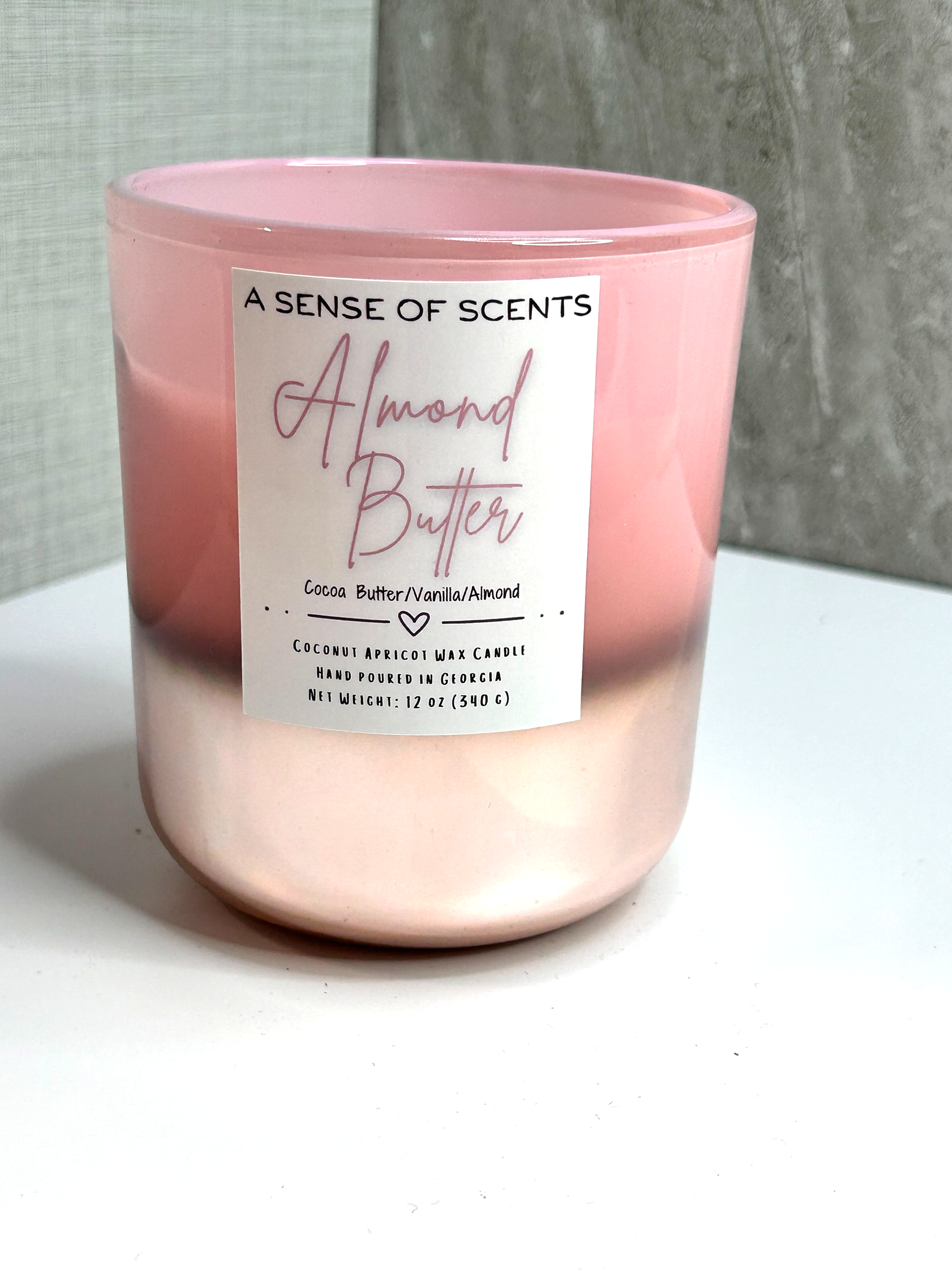 Pink candle labeled 'Almond Butter' on a white surface