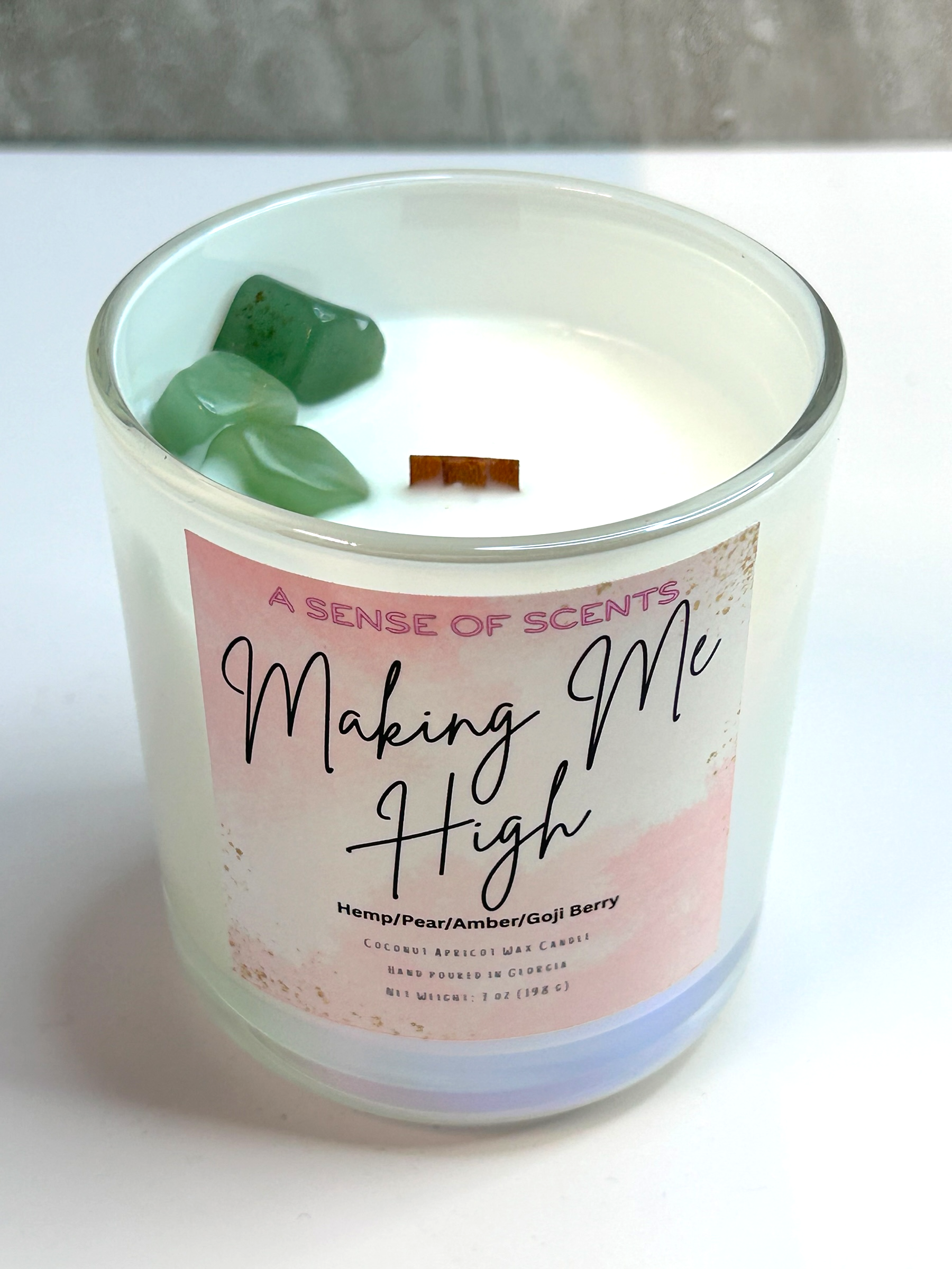 Candle in a glass jar labeled Making Me High on a white surface