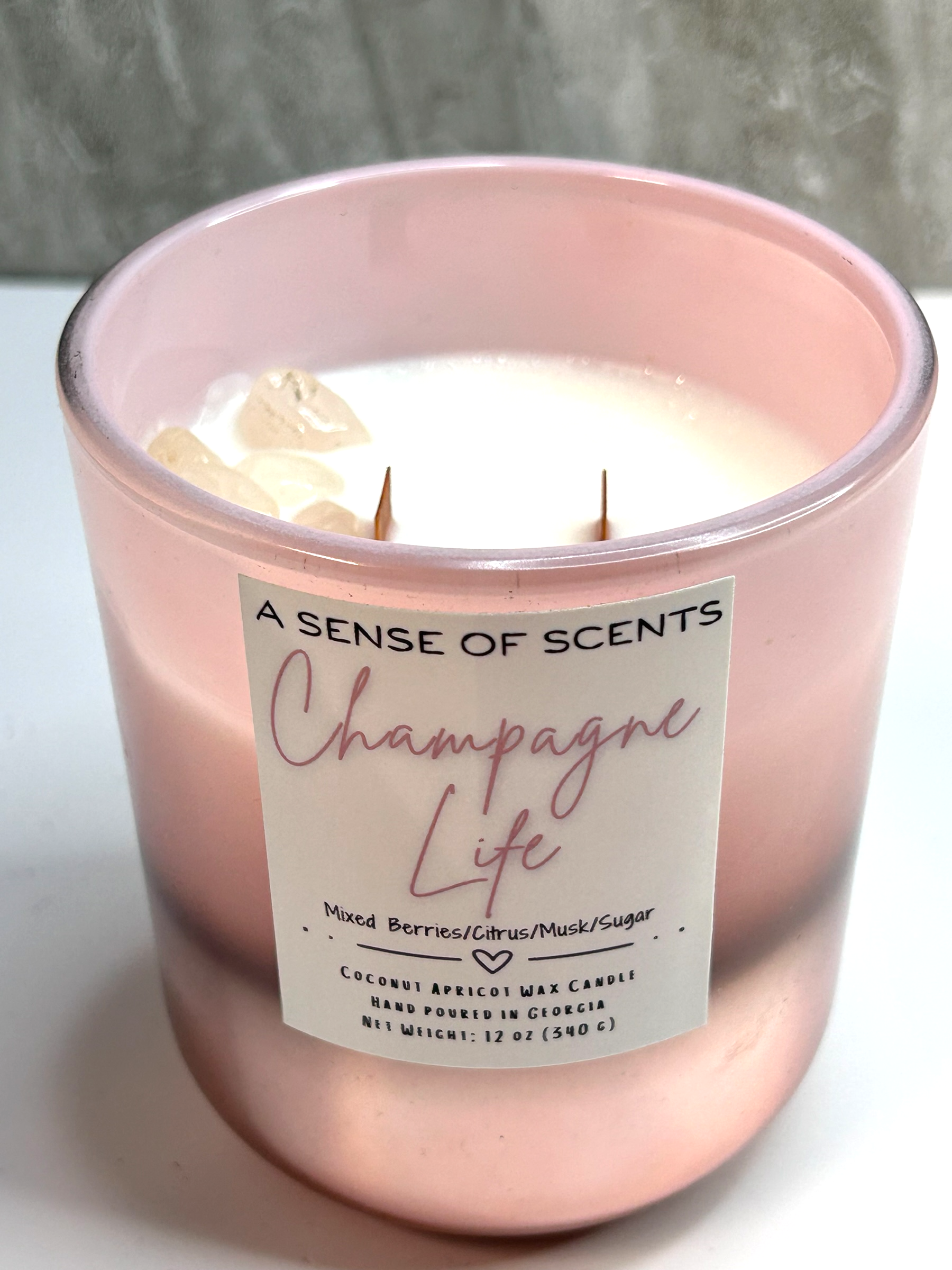 Pink candle labeled 'Champagne Life' by A Sense of Scents on a white surface.