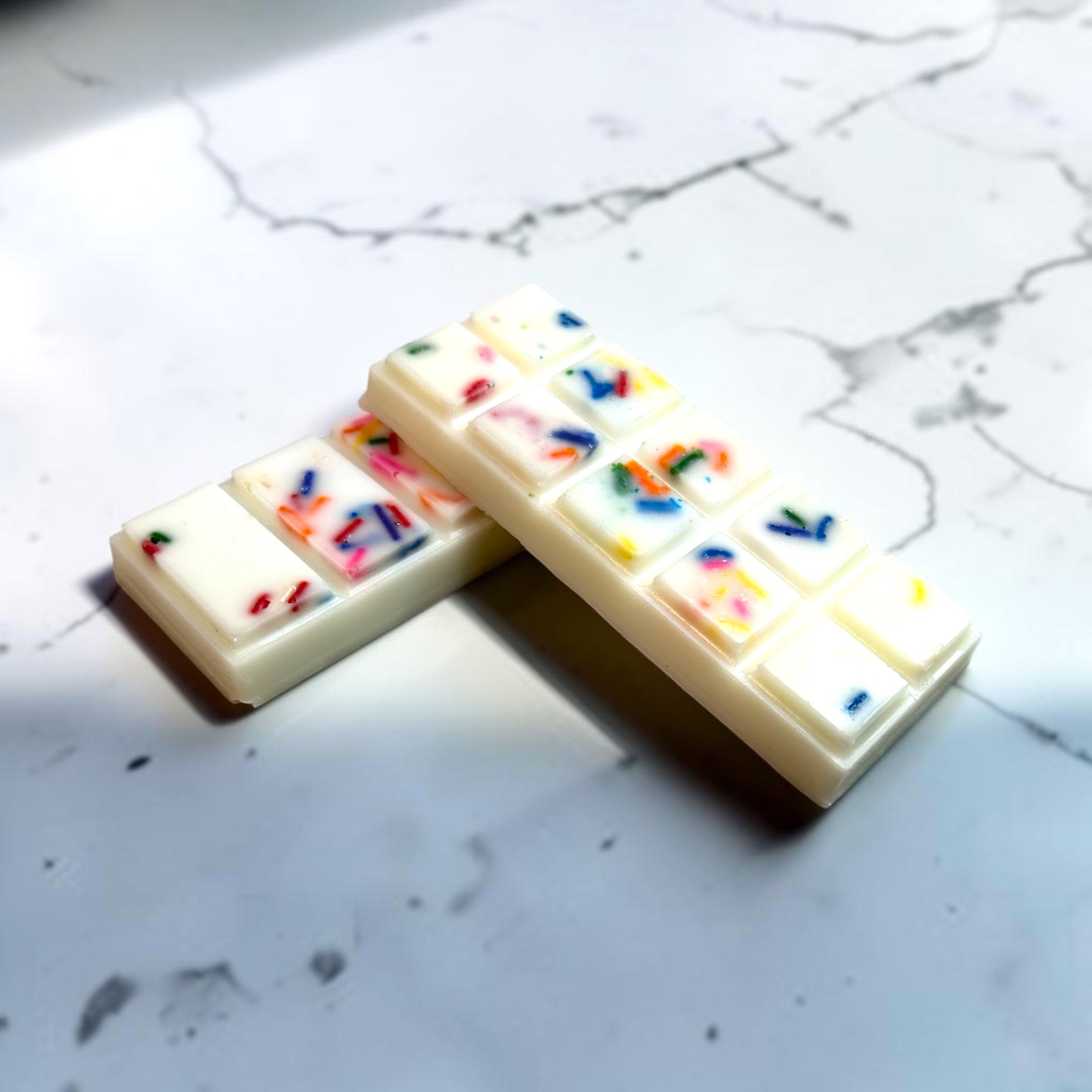 Two white vegan melting wax bars with colorful sprinkles on a marble surface