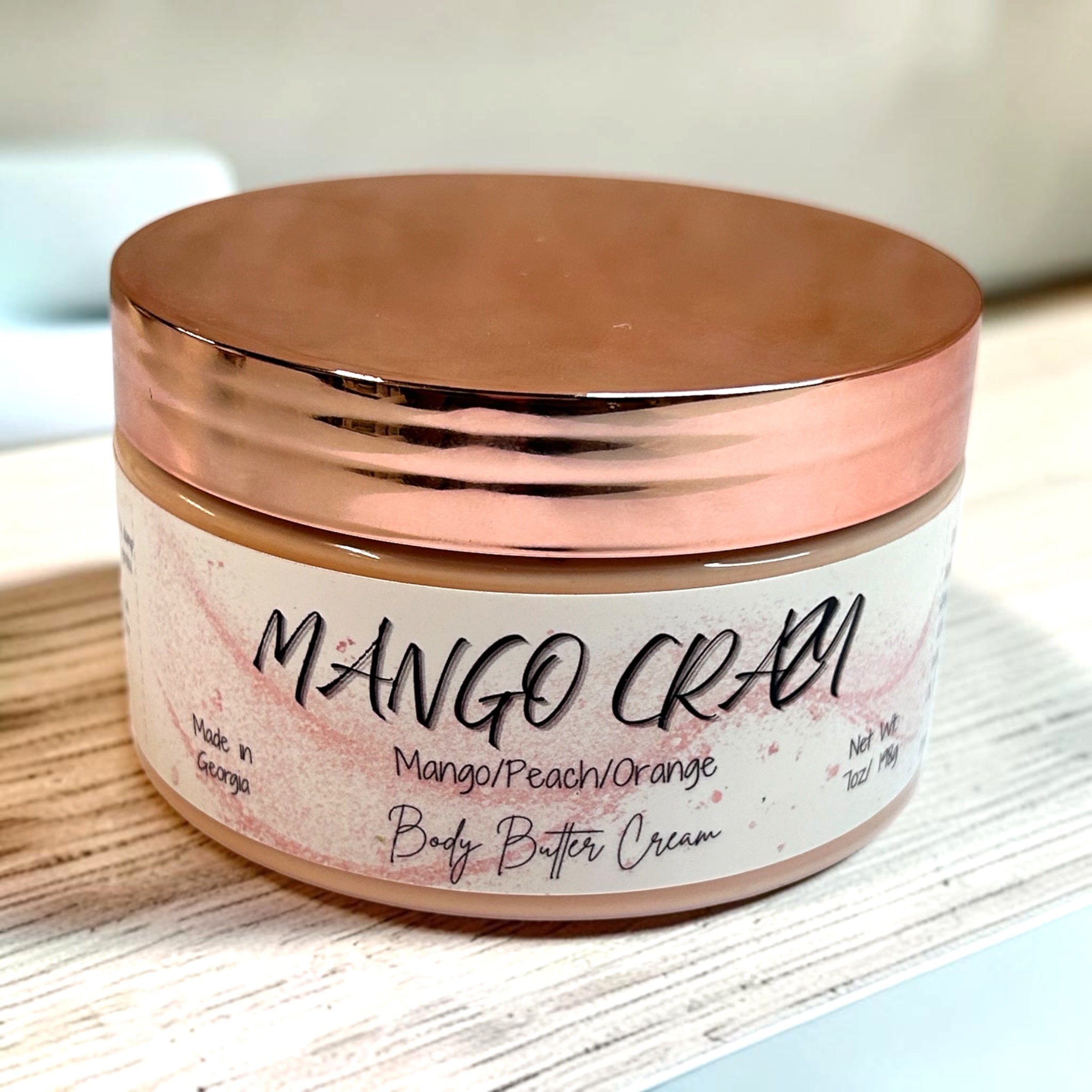 Jar of Mango Crazy body butter cream with a rose gold lid on a light wooden surface.
