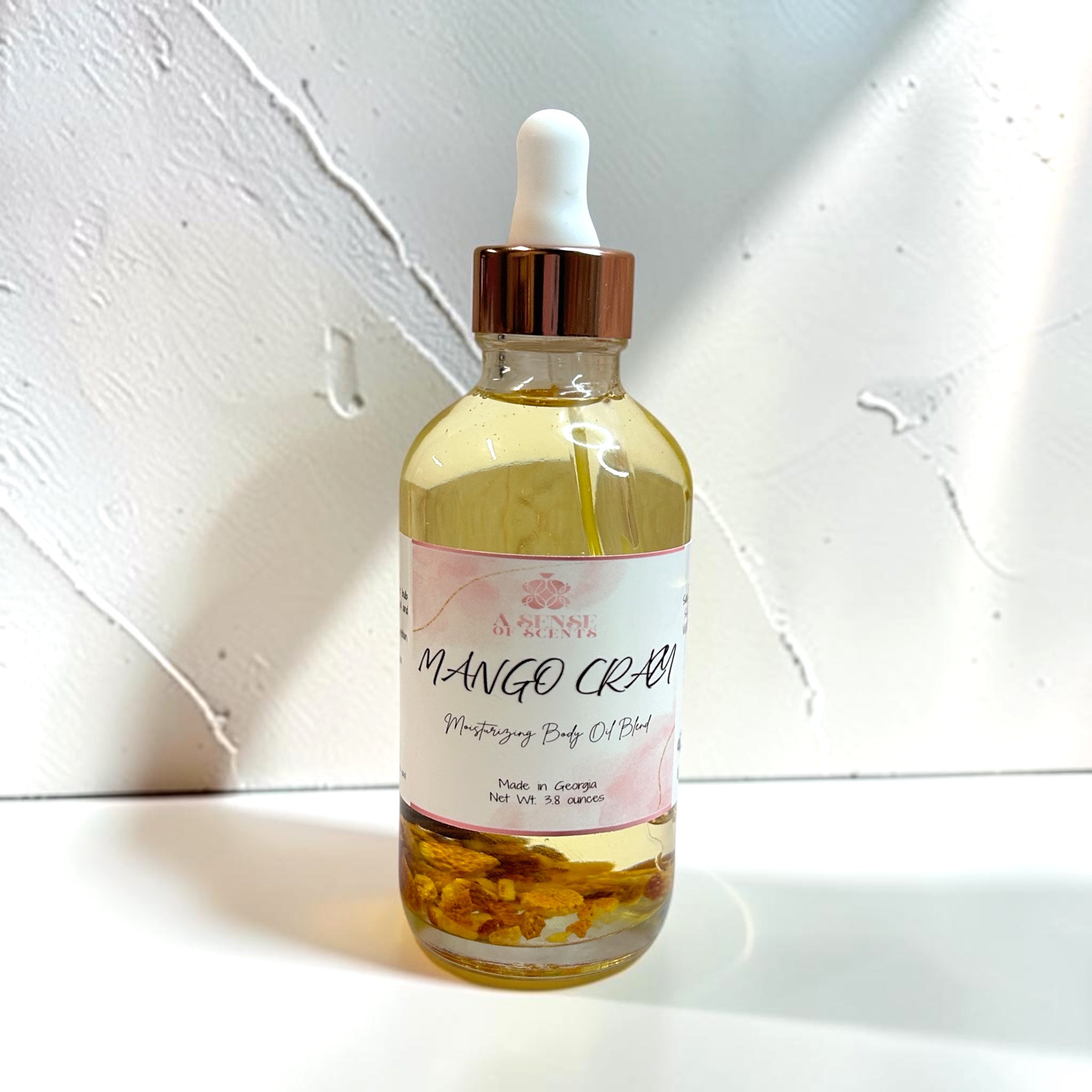Bottle of Mango Crush moisturizing body oil with a dropper on a light background