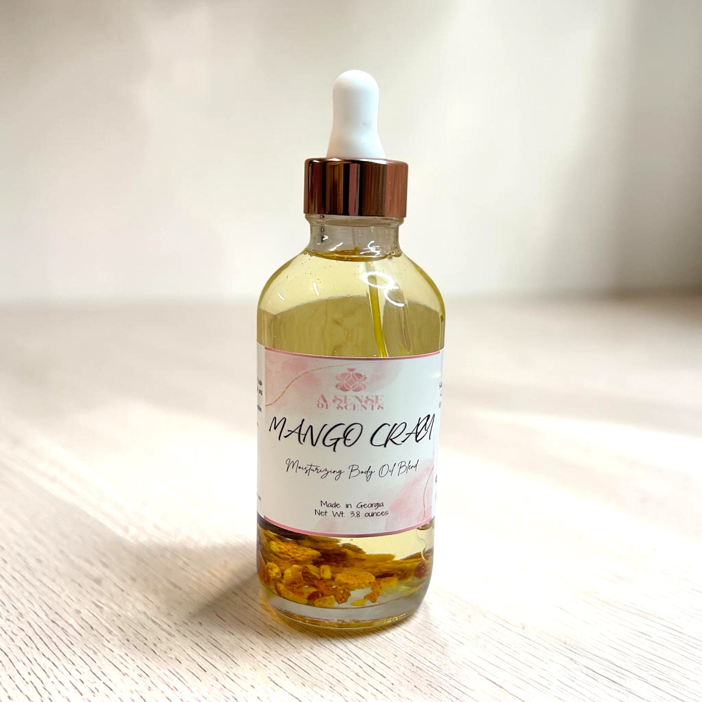 Bottle of Mango Créme body oil with dropper on a light wooden surface
