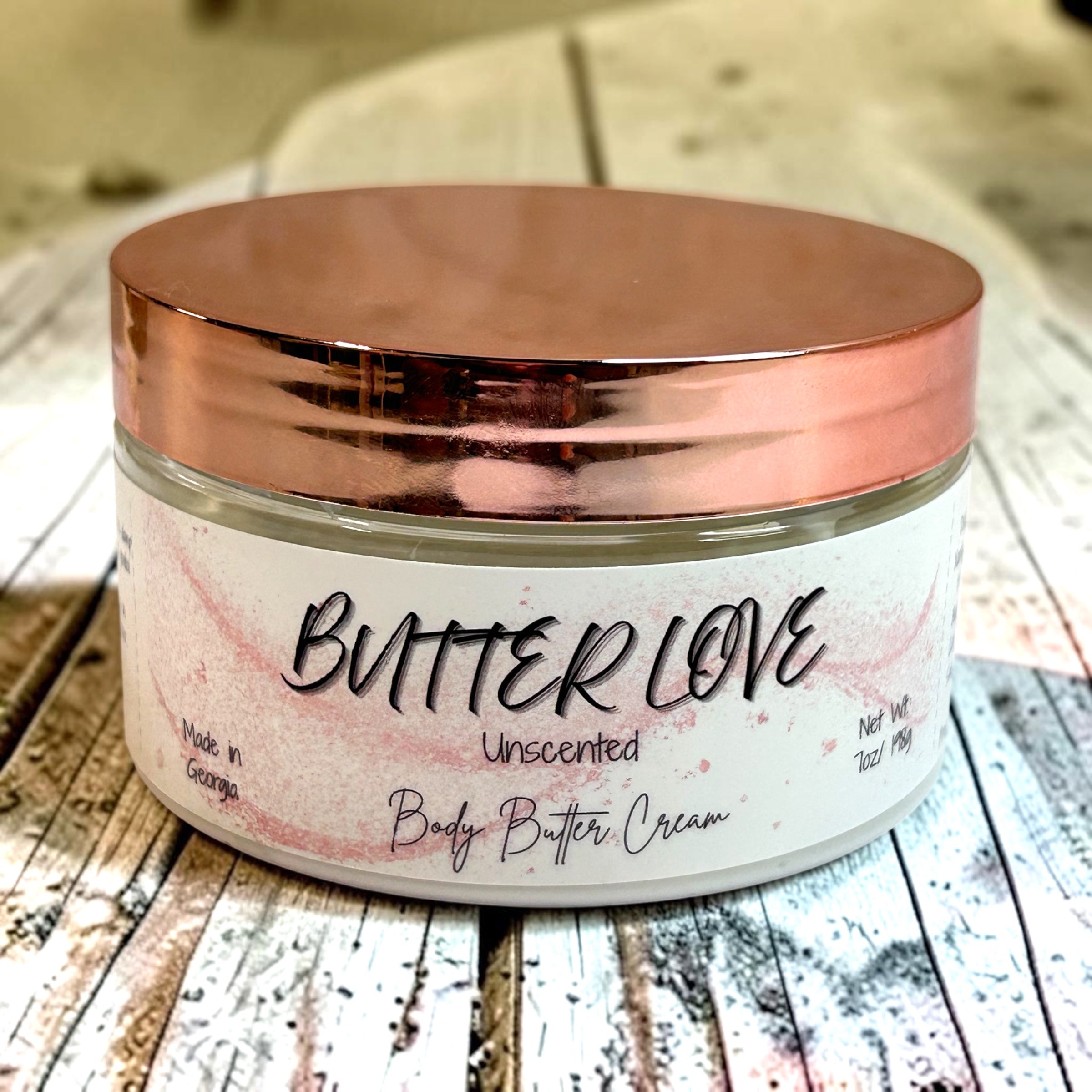 Jar of Butter Love unscented body butter cream with a rose gold lid on a wooden surface.