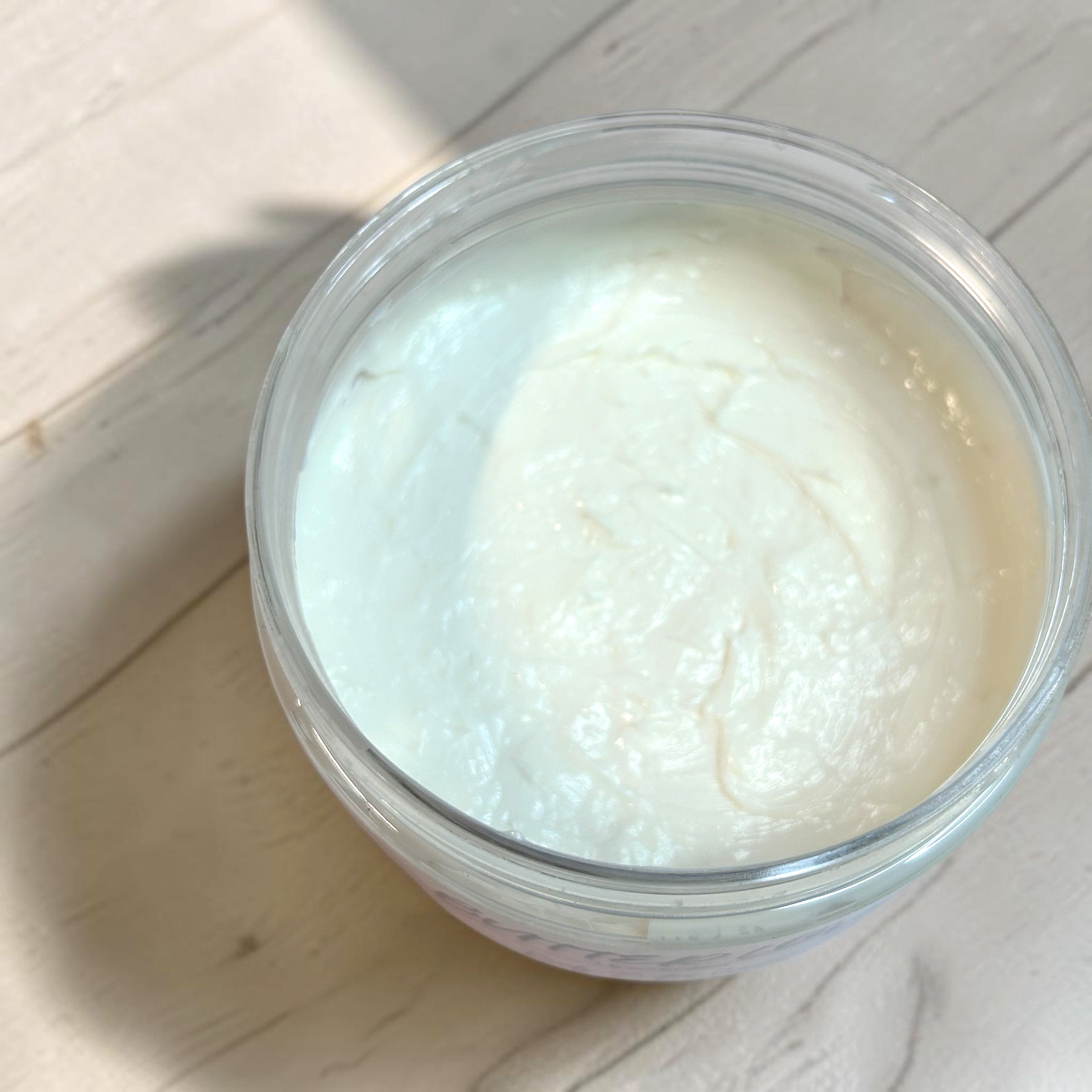 Jar of Butter Love unscented body butter cream with a rose gold lid on a wooden surface.