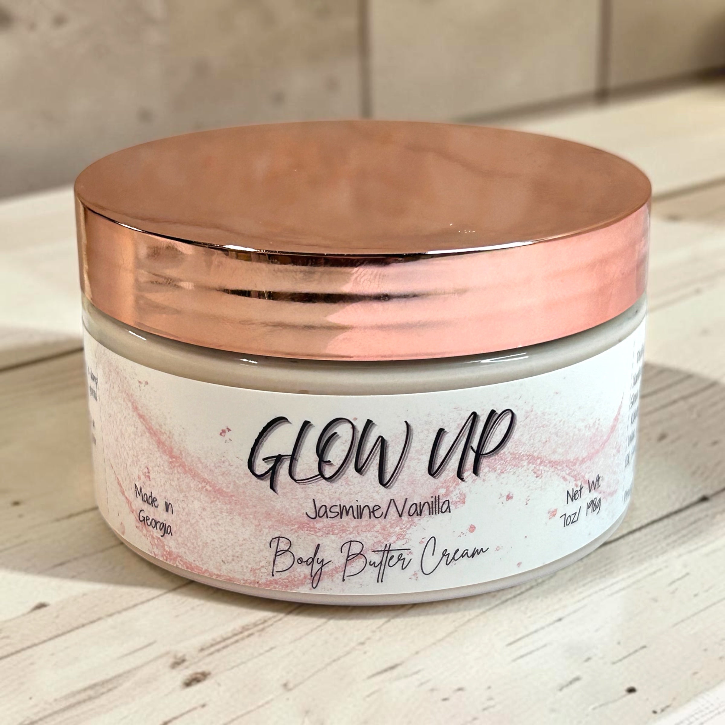 Jar of 'Glow Up' body butter cream with a rose gold lid on a wooden surface.