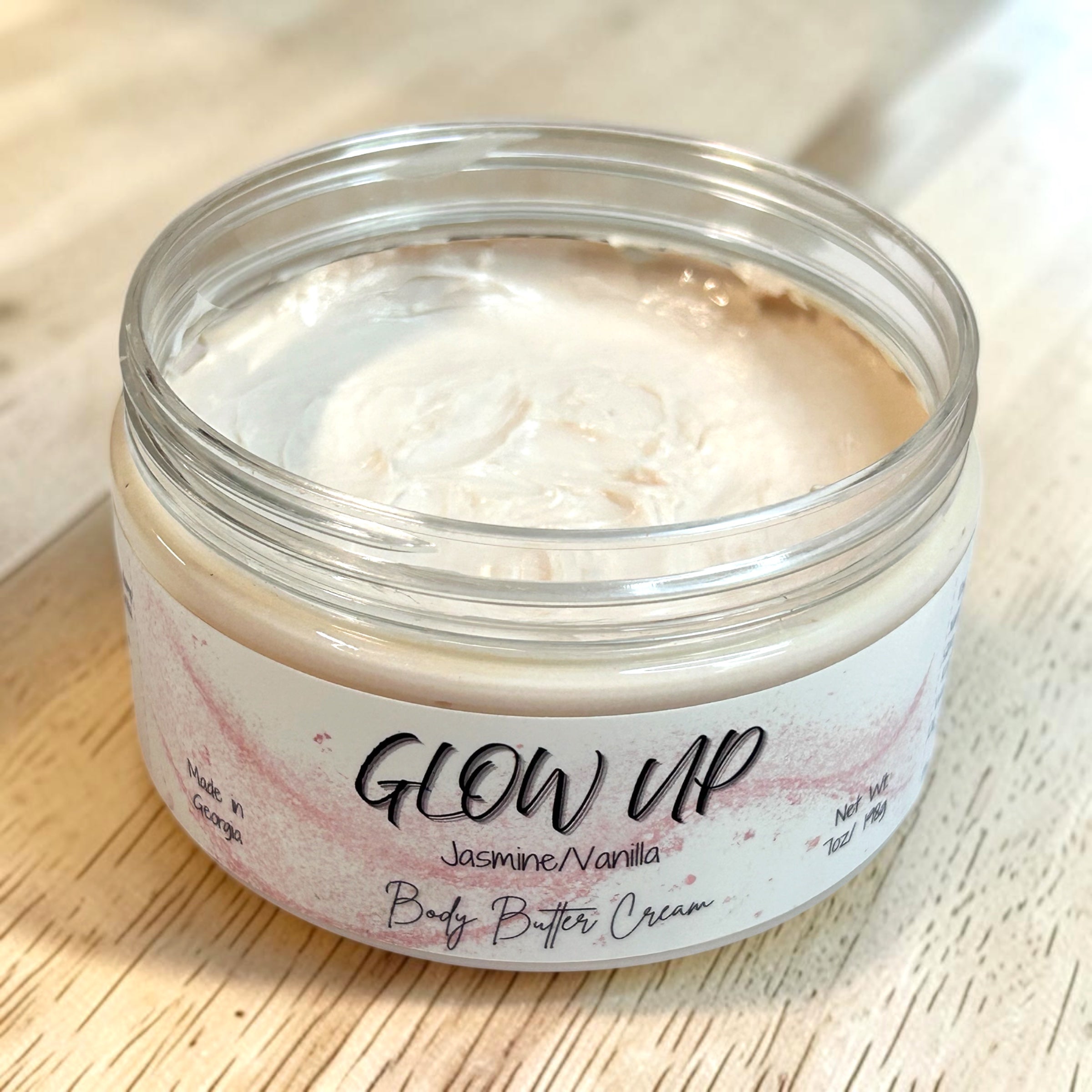 Jar of 'Glow Up' body butter cream on a wooden surface