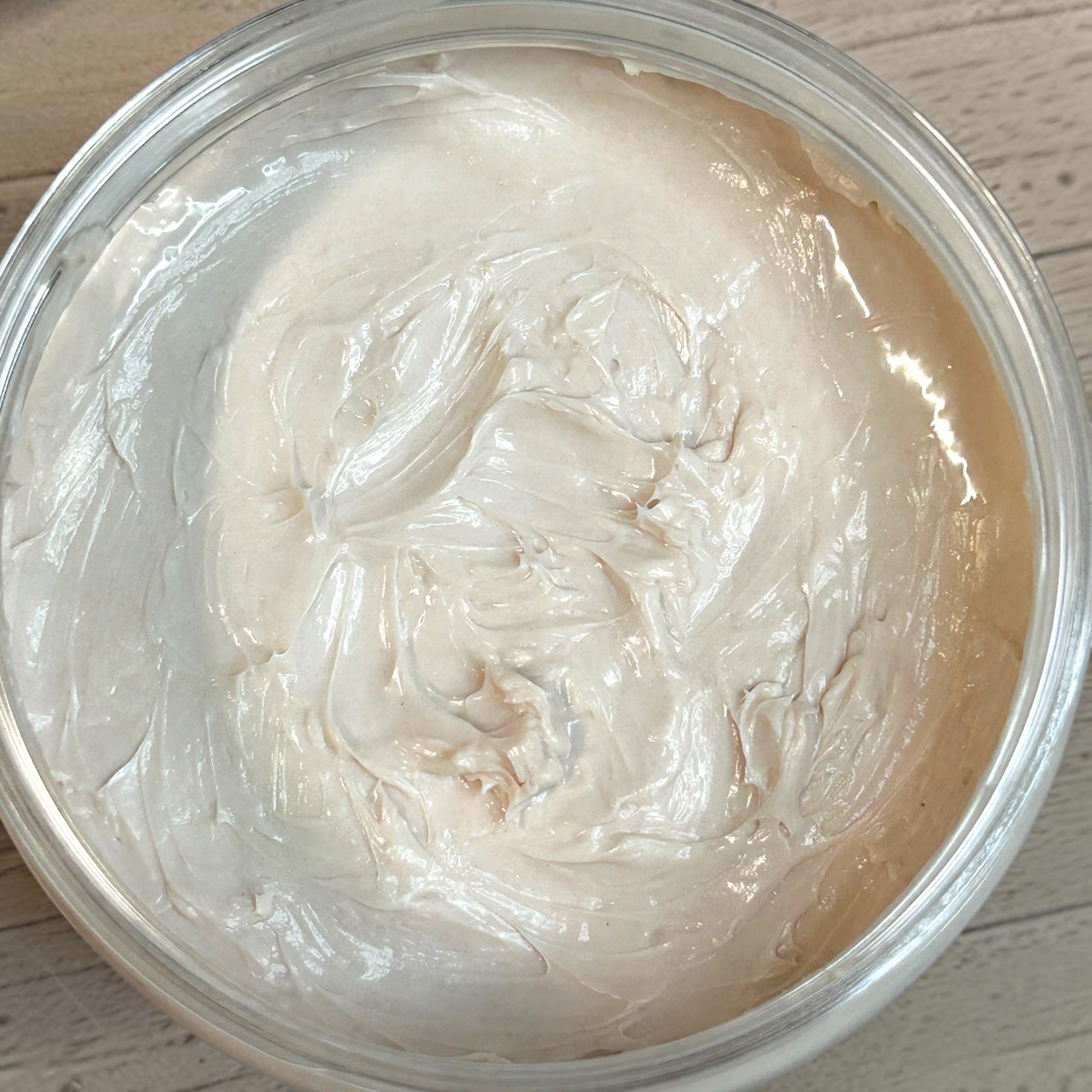 Close-up of a container filled with light-colored cream or paste on a wooden surface.