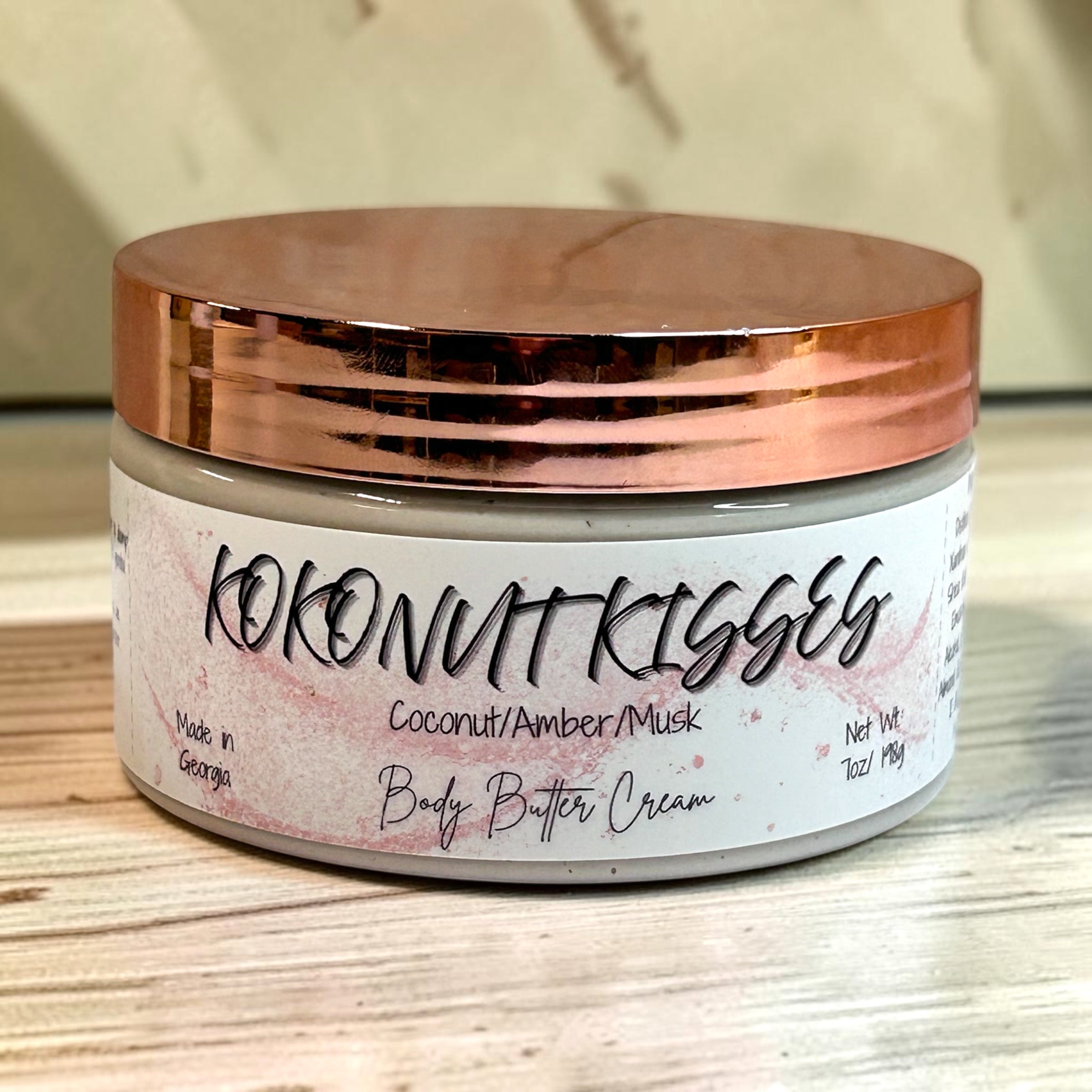 Jar of 'Kokonut Kisses' body butter cream with a rose gold lid on a wooden surface.